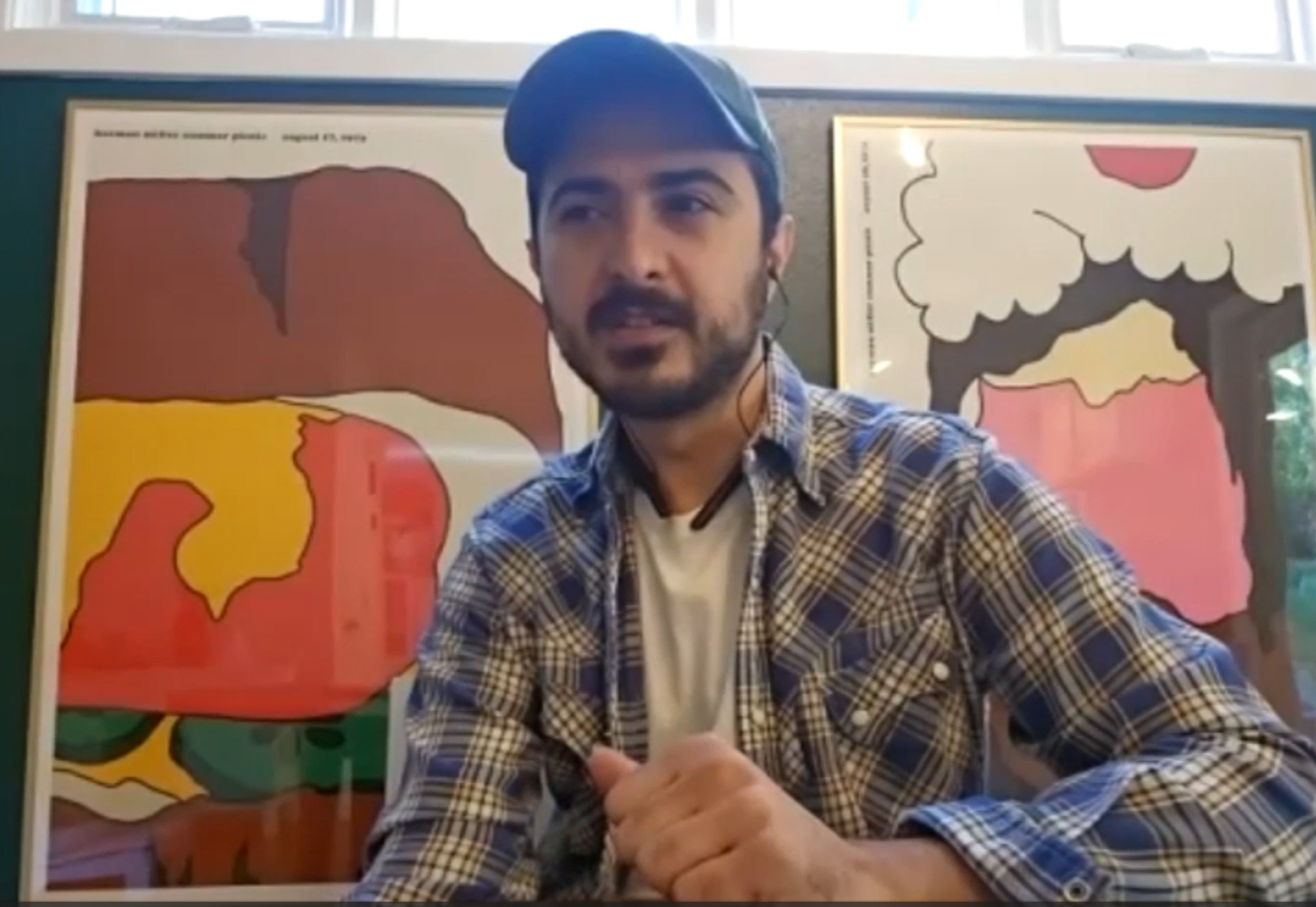 A screenshot from the video shows Farbodd Ganjifard in his dorm room wearing a plaid shirt white t shirt and a baseball cap